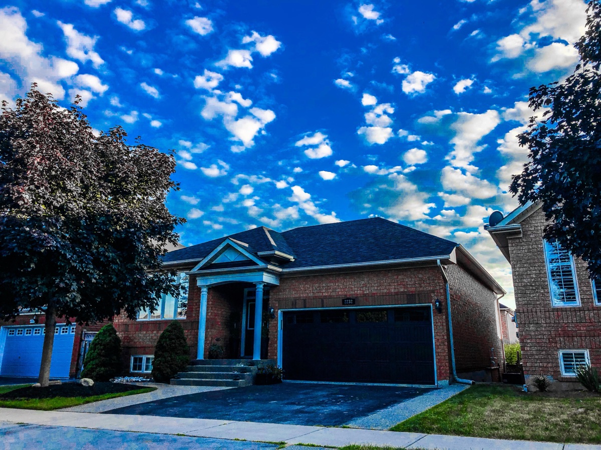Brick bungalow with a freshly installed dark shingle roof under a bright sky