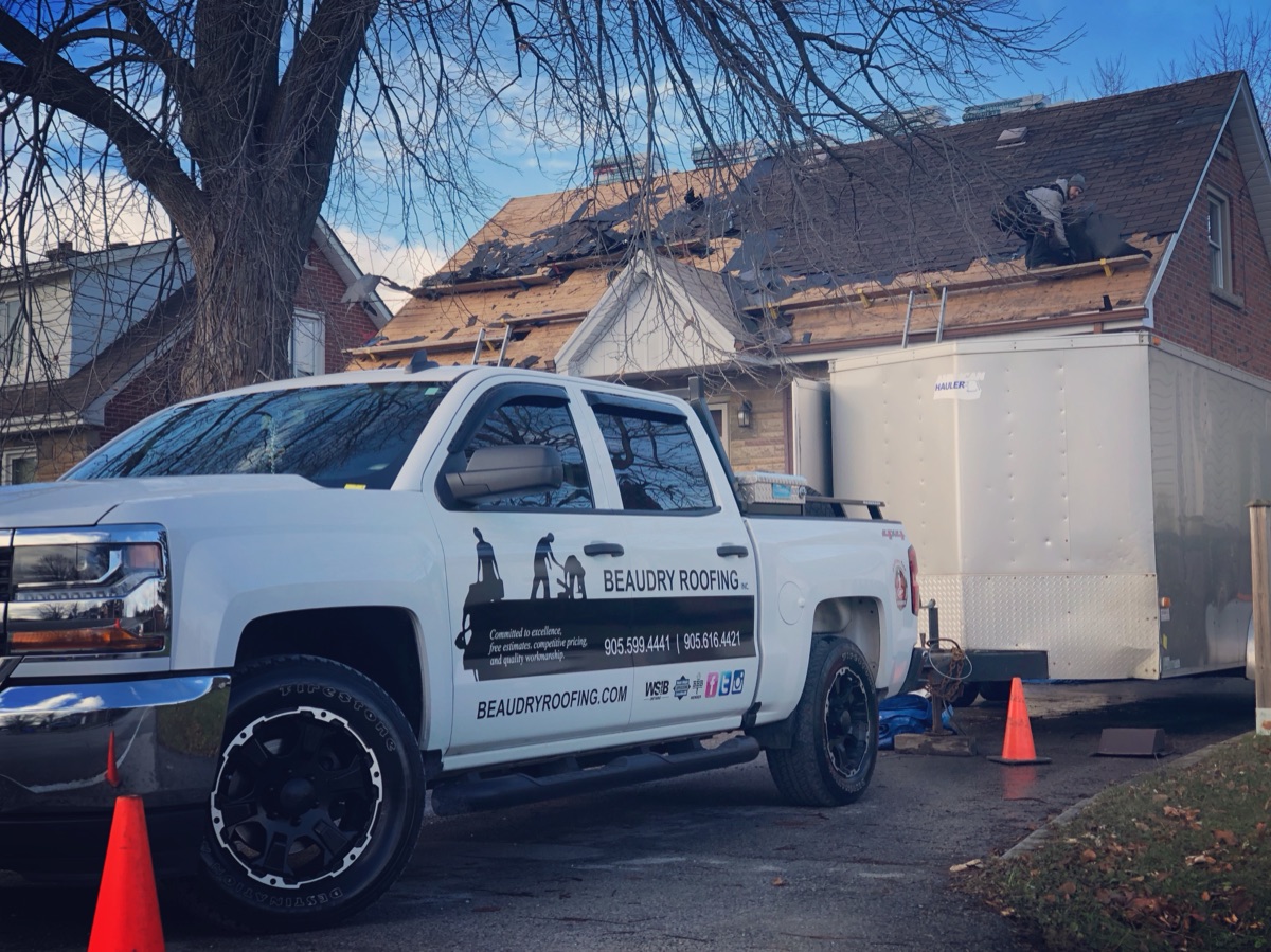 Beaudry truck and trailer at a full roof replacement with the crew mid tear-off