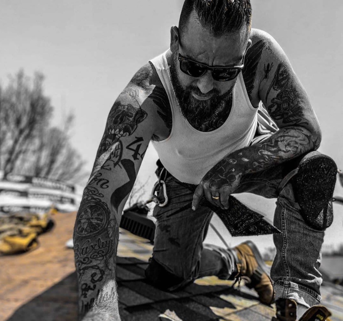 Justin Beaudry, owner of Beaudry Roofing, kneeling on a shingle roof mid-job