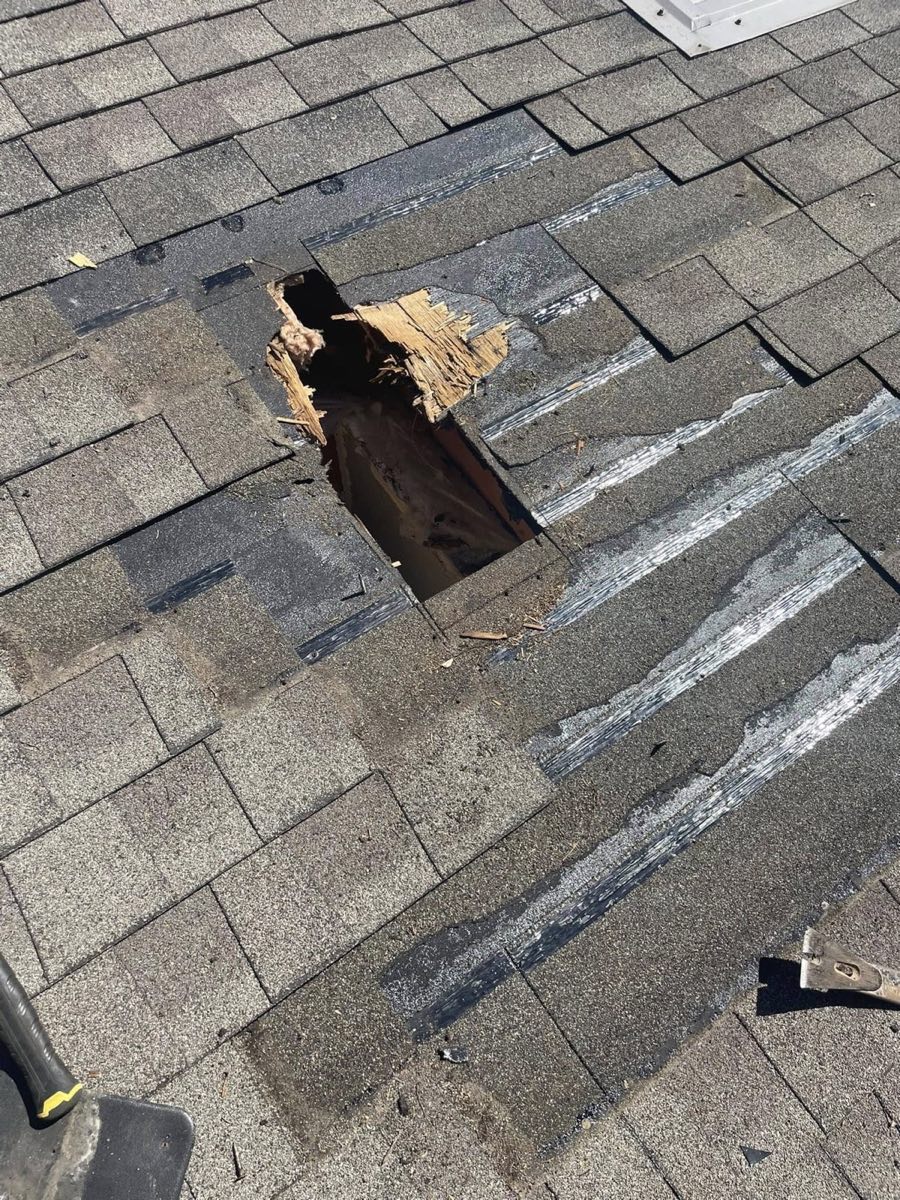 Roof with torn shingles and a hole exposing rotted decking, before repair