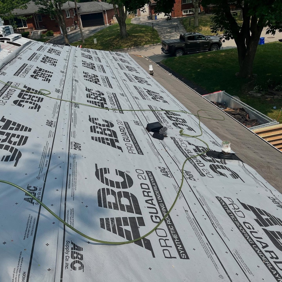 Large roof covered in synthetic underlayment during a re-roof, Beaudry truck in the driveway below